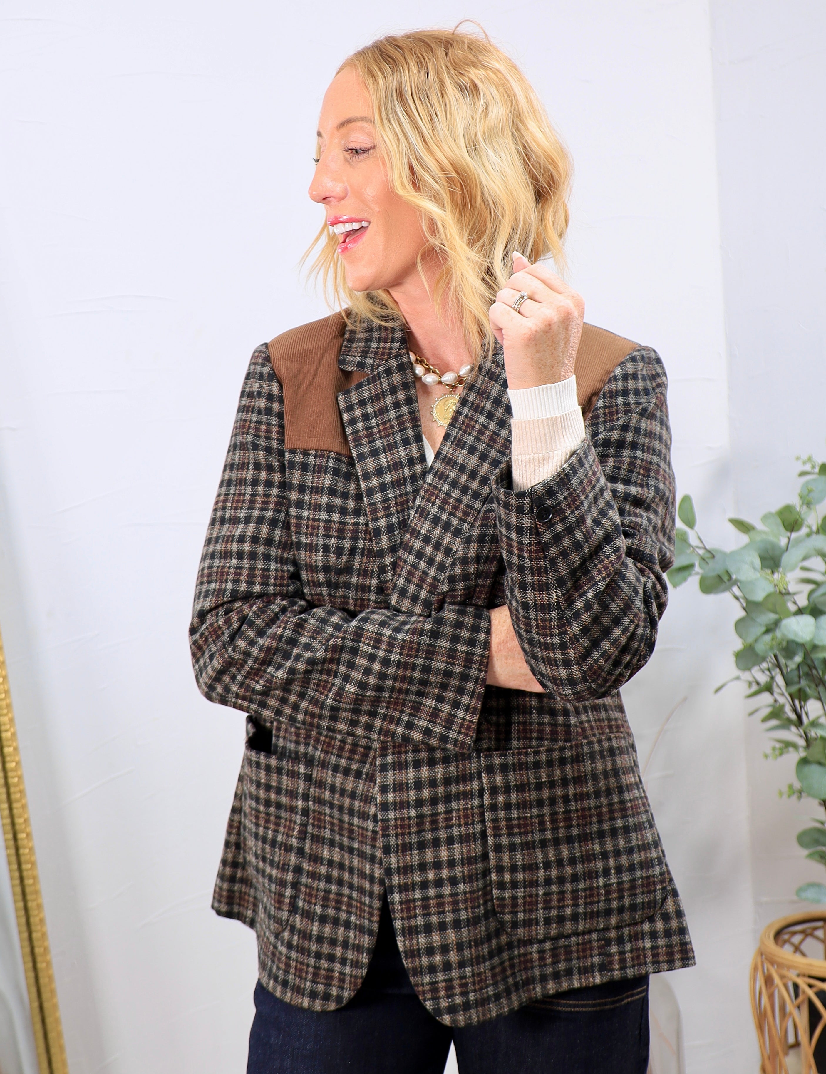 Woman wearing a brown plaid blazer with suede shoulder yoke panels over a cream top and dark jeans