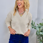 Beige v-neck knit sweater styled with dark blue jeans and layered pearl and gold coin necklace.