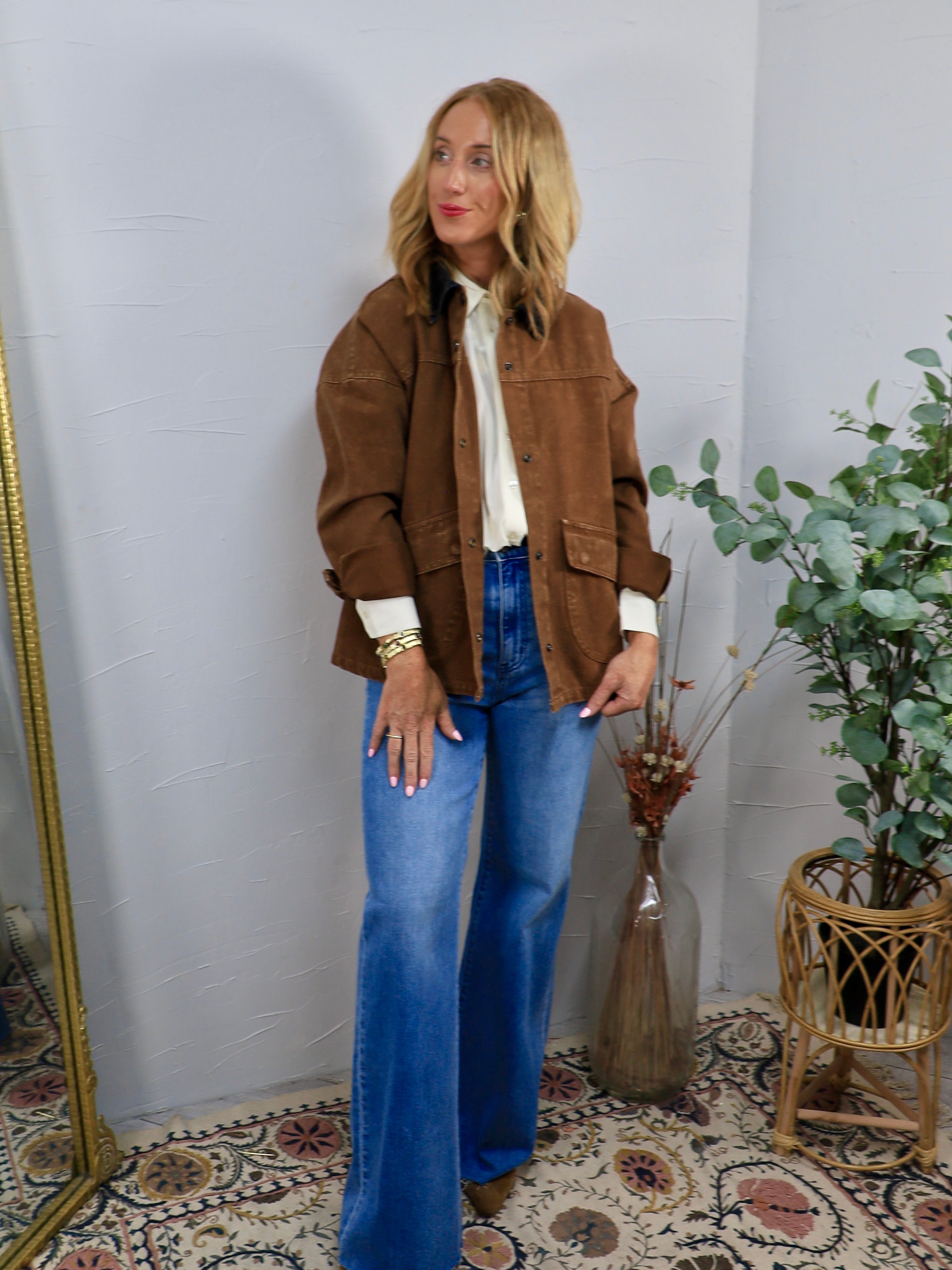 Oversized brown barn jacket styled open over cream blouse and wide-leg blue jeans with brown boots.