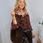 Woman wearing a dark brown paisley off-the-shoulder long sleeve blouse with a large brown studded tote bag