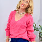 Woman wearing a bright hot pink V-neck fluffy knit sweater with dark wash jeans and layered gold jewelry
