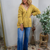 Oversized chartreuse button-front cardigan with front pockets, styled with wide-leg blue jeans and layered gold necklaces.