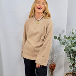 Oversized camel beige crewneck sweater with ribbed cuffs, styled with black wide-leg trousers and pearl necklace.