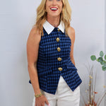 Blue and black gingham sleeveless vest with gold buttons and white collar, styled over white trousers.