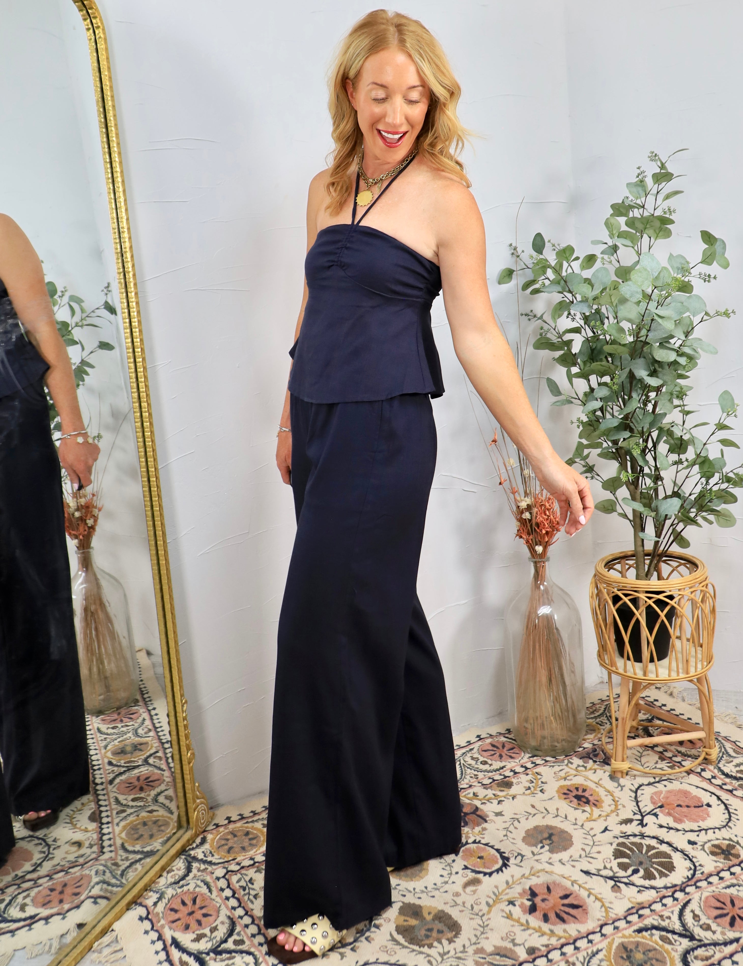 Woman wearing navy blue strapless halter top with matching wide-leg flowy pants, styled with jewelry in bohemian-decorated ro