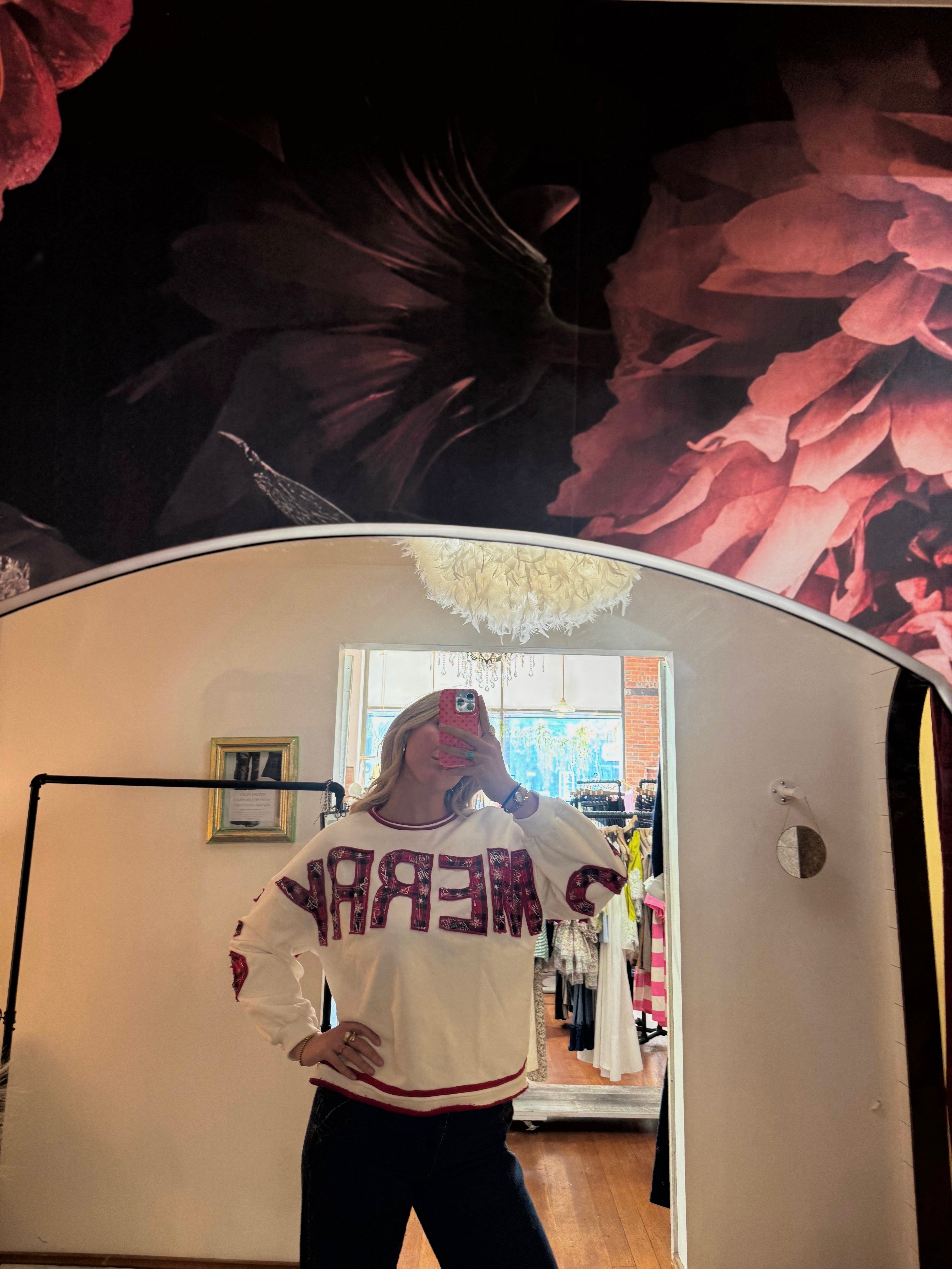 White crewneck sweatshirt with red sequin "MERRY" lettering, red striped trim, styled with dark jeans, mirror selfie.
