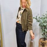 Woman wearing olive green ruched suede bomber jacket over floral sweater with dark wide-leg jeans