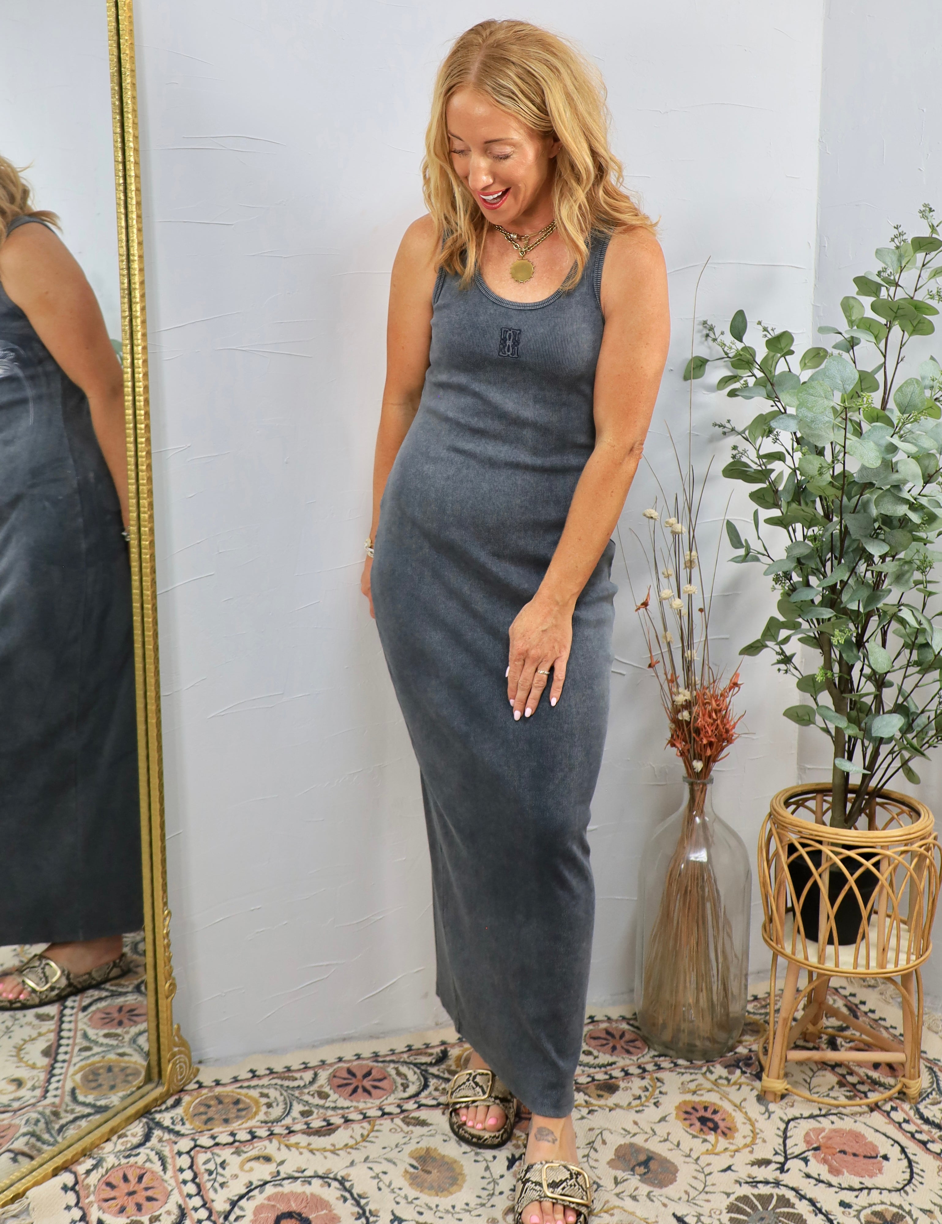 Woman wearing gray ribbed sleeveless maxi dress with layered necklaces, styled with strappy sandals in boho-chic setting.