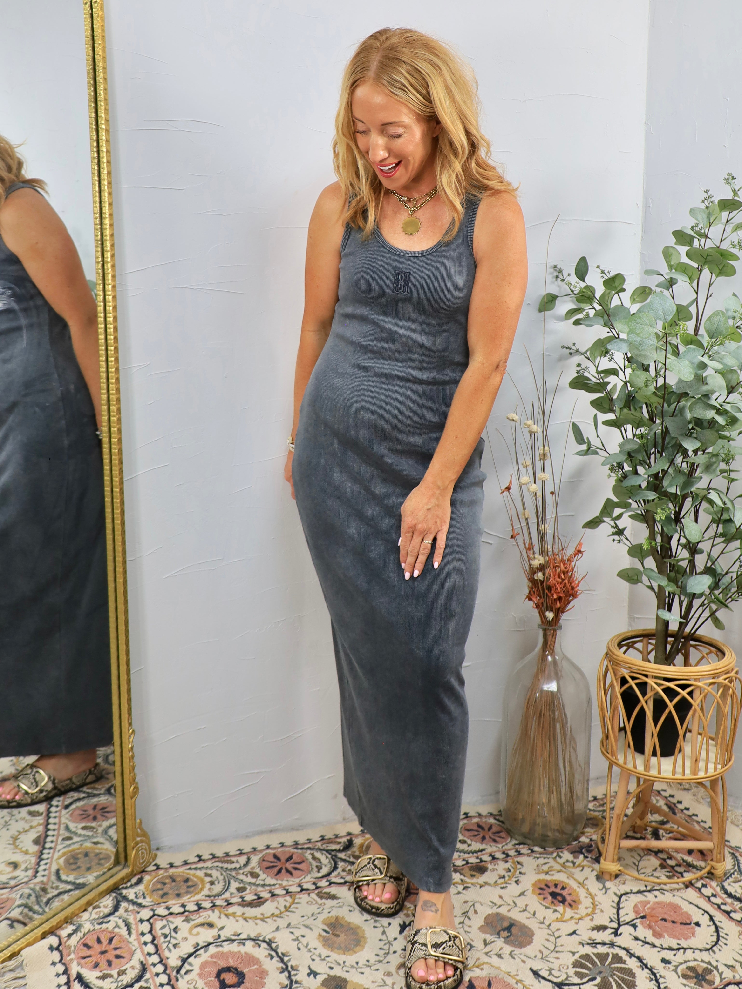 Woman wearing gray ribbed sleeveless maxi dress with layered necklaces, styled with strappy sandals in boho-chic setting.