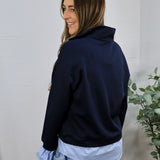 Navy blue pullover sweatshirt layered over light blue collared shirt, styled with light wash jeans, back view.