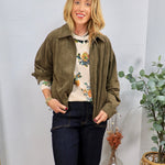 Olive green suede zip-up bomber jacket with ruched sleeves, worn open over a floral sweater with dark jeans.