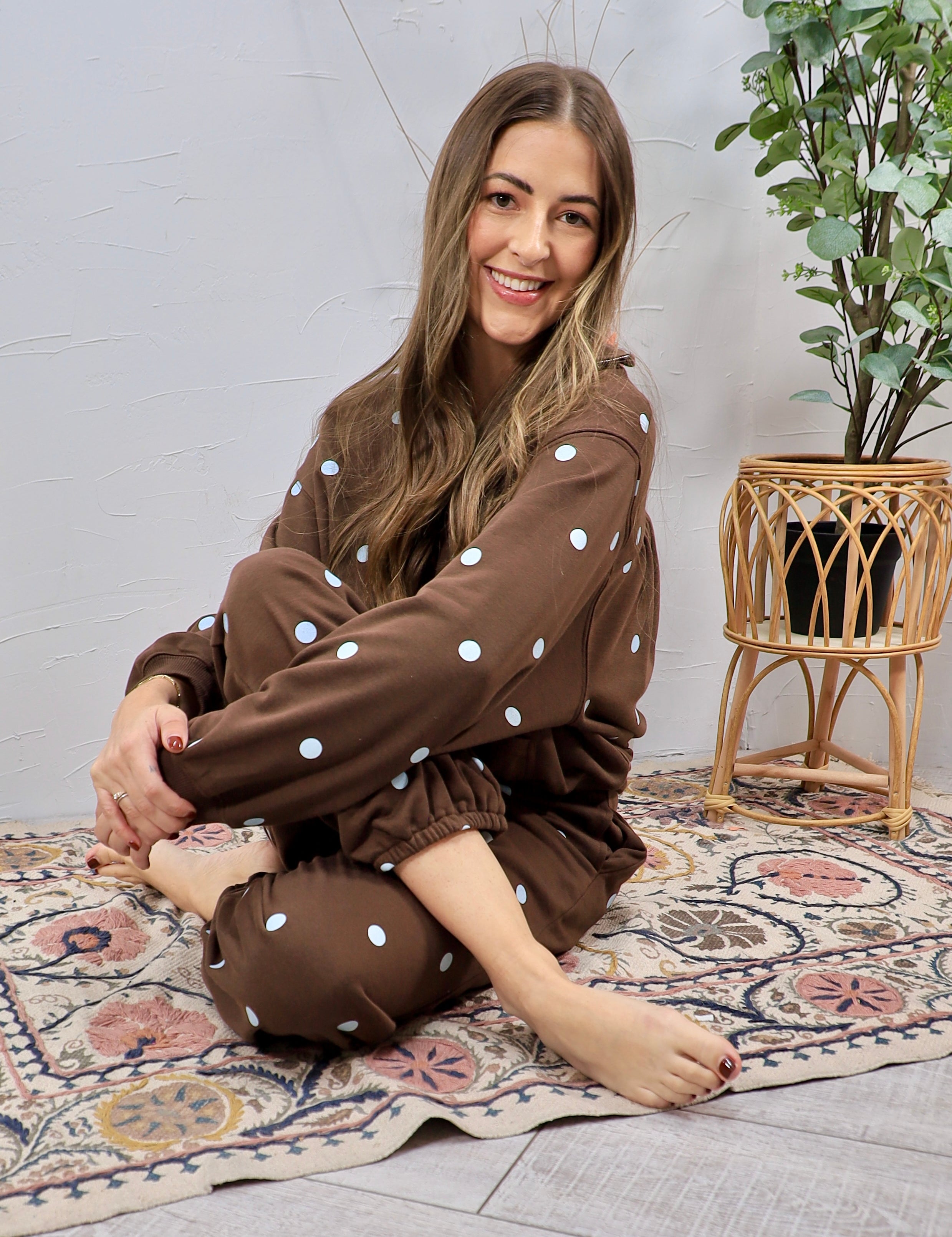 Woman seated cross-legged wearing chocolate brown polka dot matching sweatshirt and jogger set