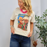 Woman wearing cream Cowboys and Indians graphic tee with pink statement necklace and denim shorts in casual styling.