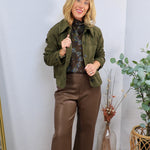 Olive green suede cropped jacket with button closure, worn over floral blouse and brown wide-leg pants.