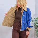 Blue denim jacket with tan sherpa teddy lining and collar, shown open, styled over brown turtleneck and pants.