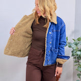 Blue denim jacket with tan sherpa teddy lining and collar, shown open, styled over brown turtleneck and pants.