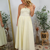 Woman wearing pale yellow strapless maxi dress with beaded halter neckline detail, styled with layered gold necklaces and wav
