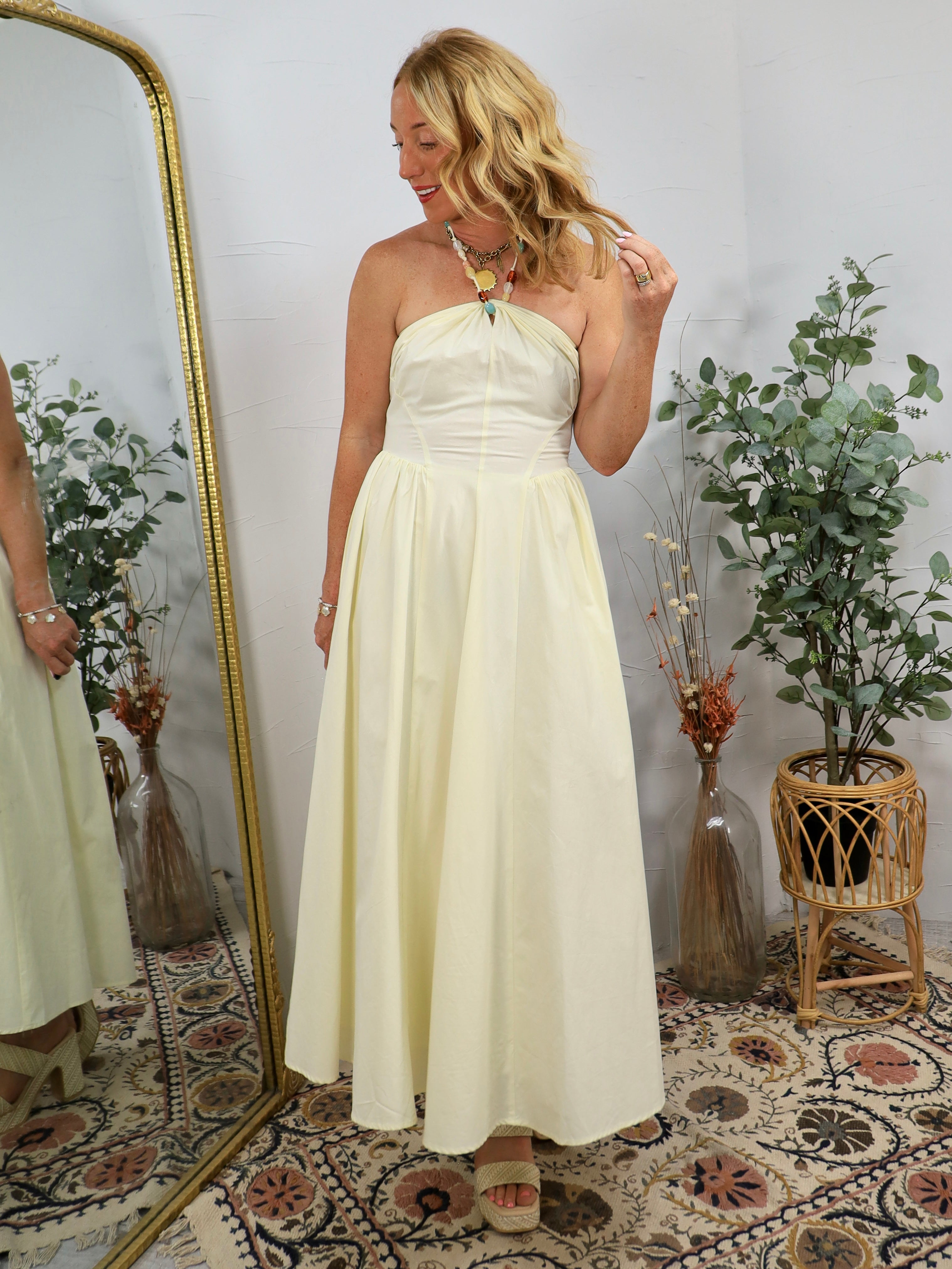 Woman wearing pale yellow strapless maxi dress with beaded halter neckline detail, styled with layered gold necklaces and wav