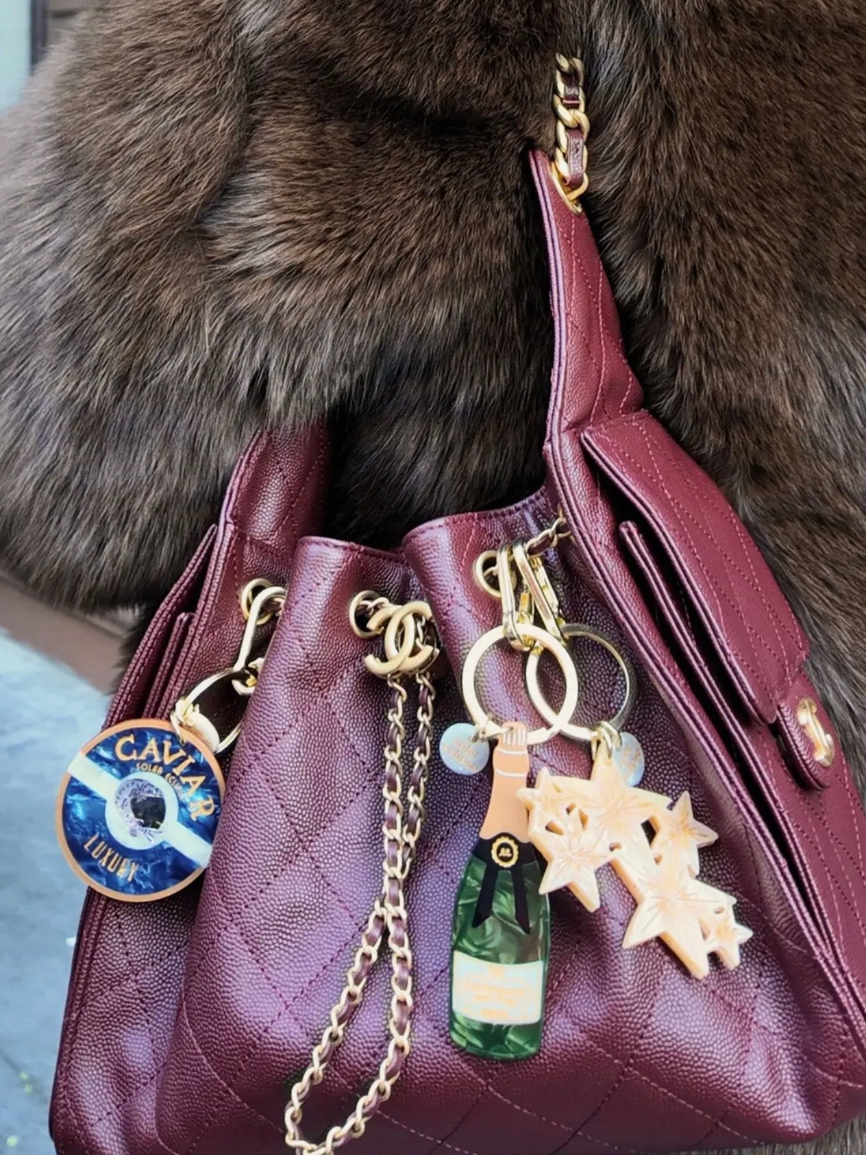 Burgundy quilted Chanel caviar leather bag with solar eclipse "Caviar Luxury" keychain, champagne bottle charm, and snowflake