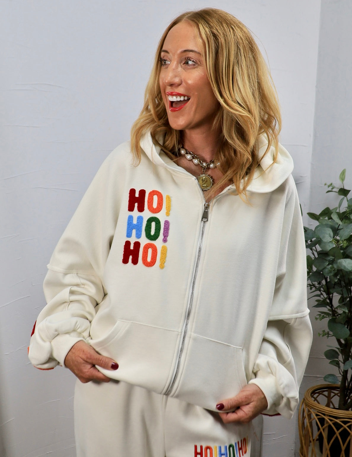 Woman wearing cream zip-up hoodie with colorful chenille HO HO HO holiday lettering on chest