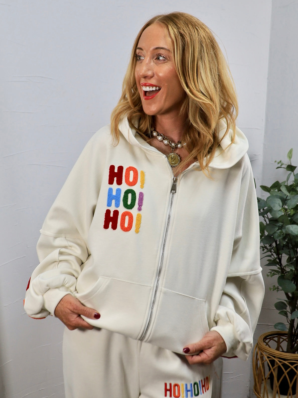 Woman wearing cream zip-up hoodie with colorful chenille HO HO HO holiday lettering on chest