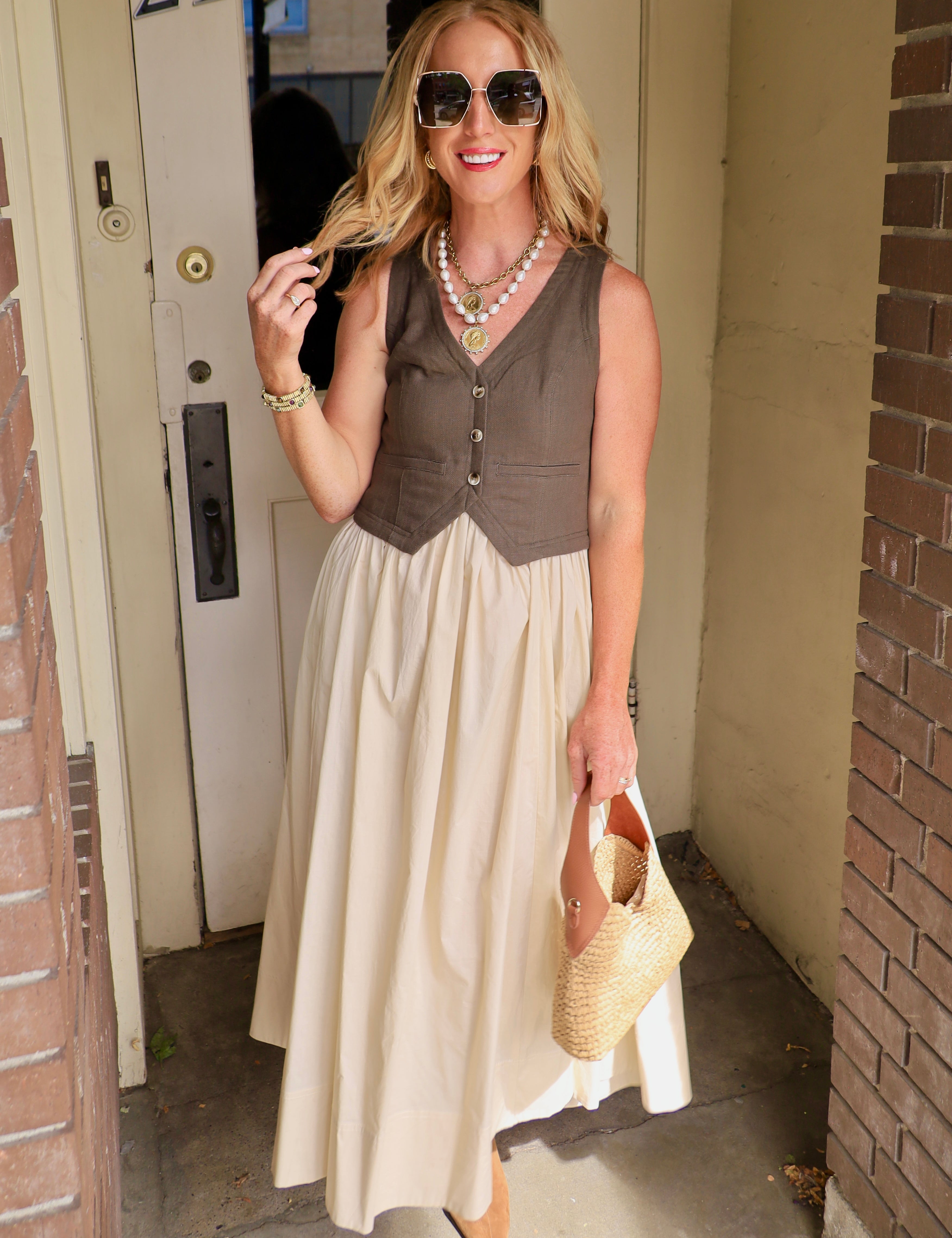 Woman wearing olive contrast vest midi dress with cream skirt, woven bag, and oversized sunglasses