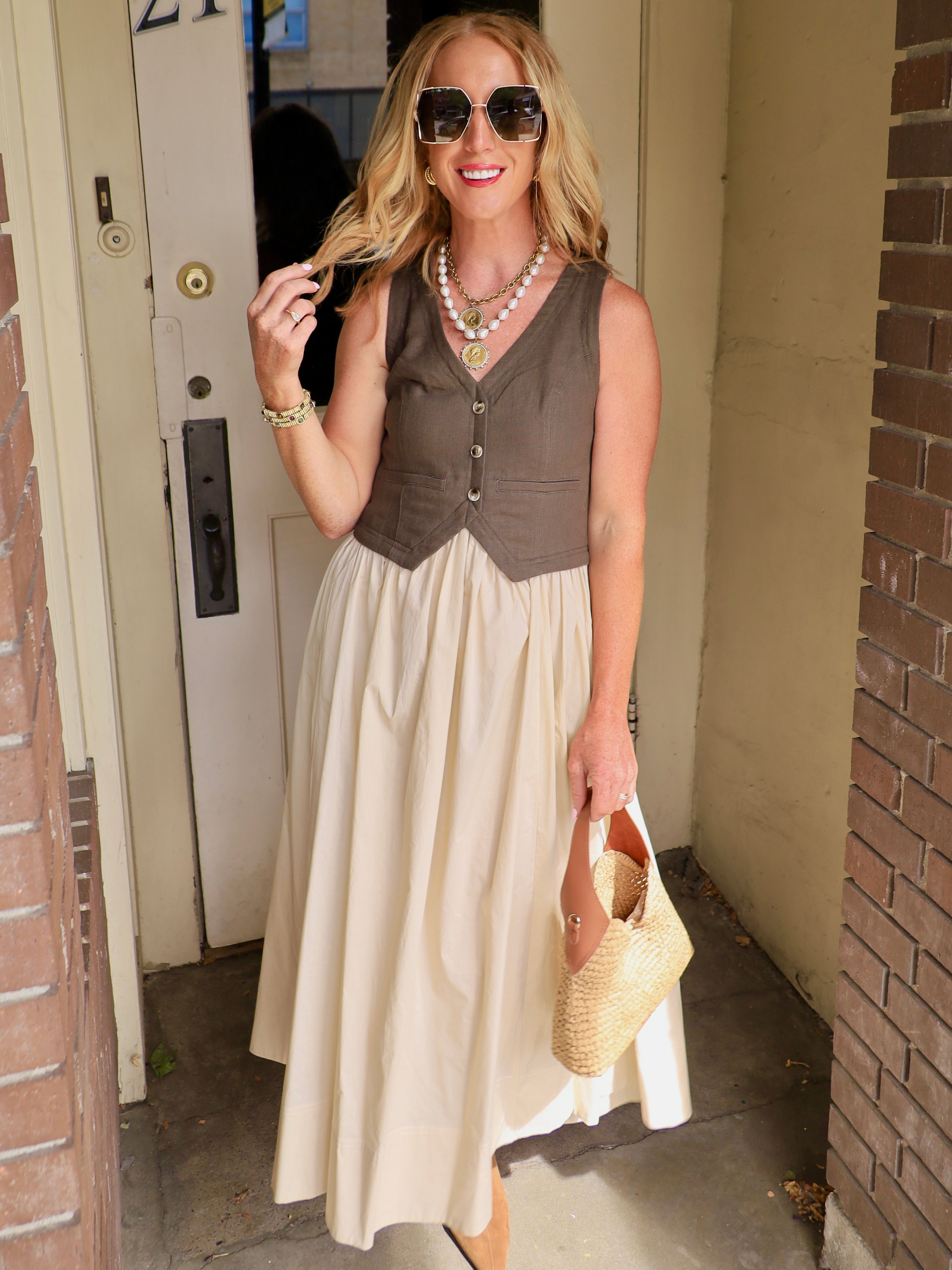 Woman wearing olive contrast vest midi dress with cream skirt, woven bag, and oversized sunglasses