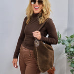 Woman wearing a chocolate brown fitted turtleneck long sleeve top with matching brown studded pants and suede hobo bag