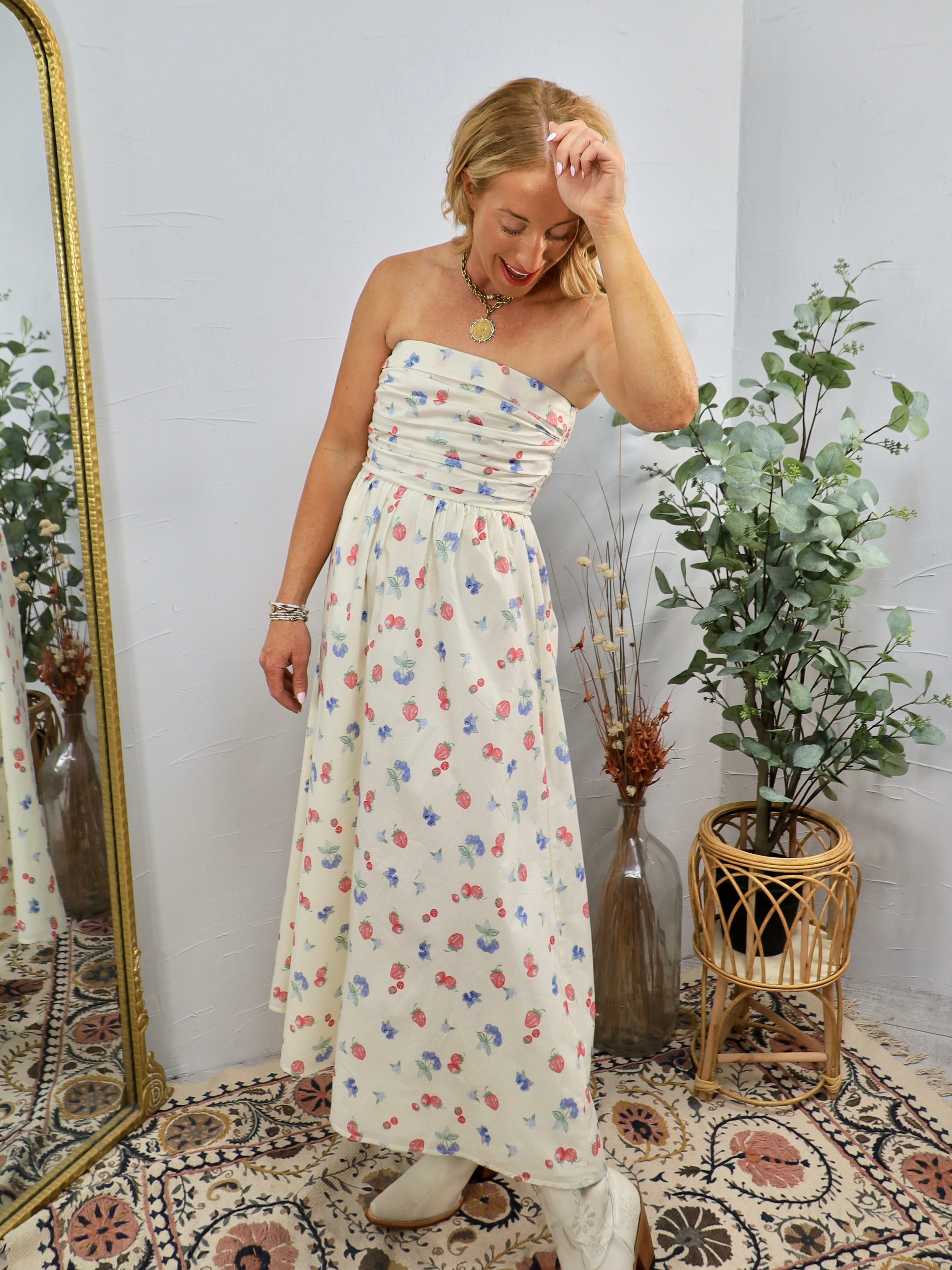 Woman wearing cream strapless midi dress with colorful floral print in styled room with plants
