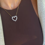 Delicate gold chain necklace with open heart pendant made of sparkling round crystal stones worn over a brown top.