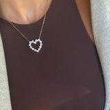 Delicate gold chain necklace with open heart pendant made of sparkling round crystal stones worn over a brown top.