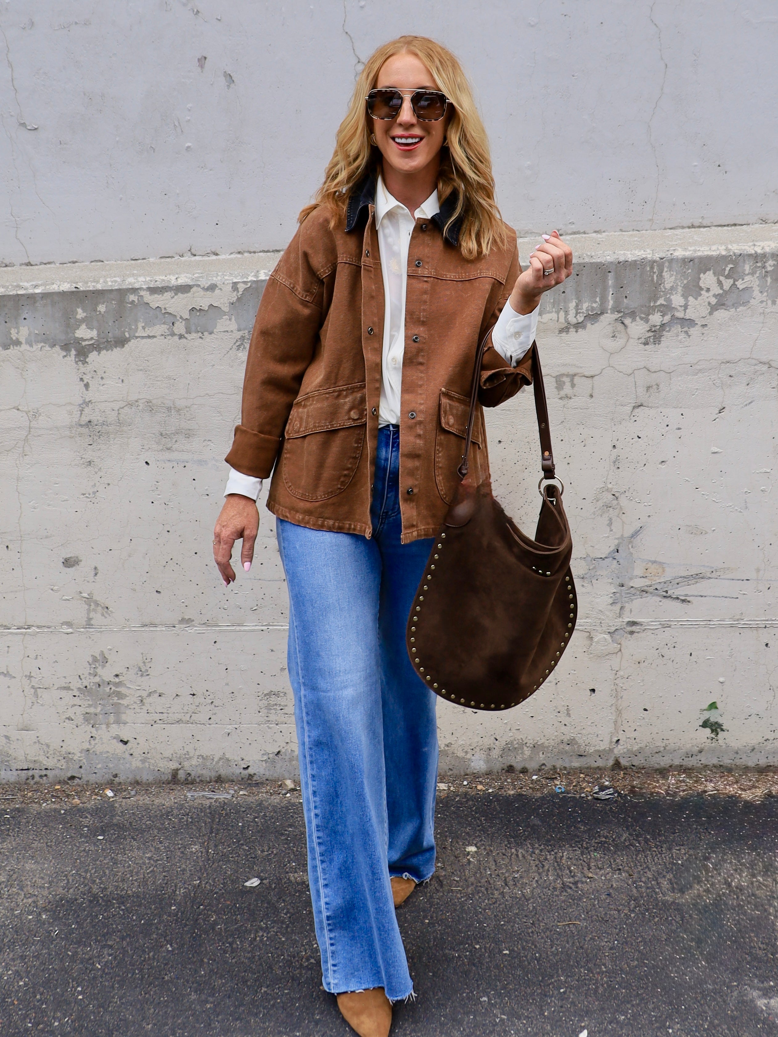 Woman wearing a caramel brown barn jacket with wide-leg jeans and a brown studded hobo bag