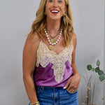 Woman wearing a purple satin spaghetti strap cami with cream lace neckline detailing and blue jeans