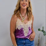 Woman wearing a purple satin spaghetti strap cami with cream lace neckline detailing and blue jeans