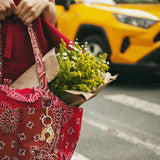 Red bandana paisley tote bag with Solar Eclipse keychain charm, styled with fresh wildflower bouquet and red outfit.
