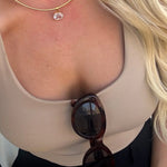 Gold snake chain necklace with oval clear crystal pendant worn against a tan neckline