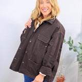 Oversized dark brown utility jacket with snap buttons, chest pocket, and sherpa lining, styled over blue jeans.