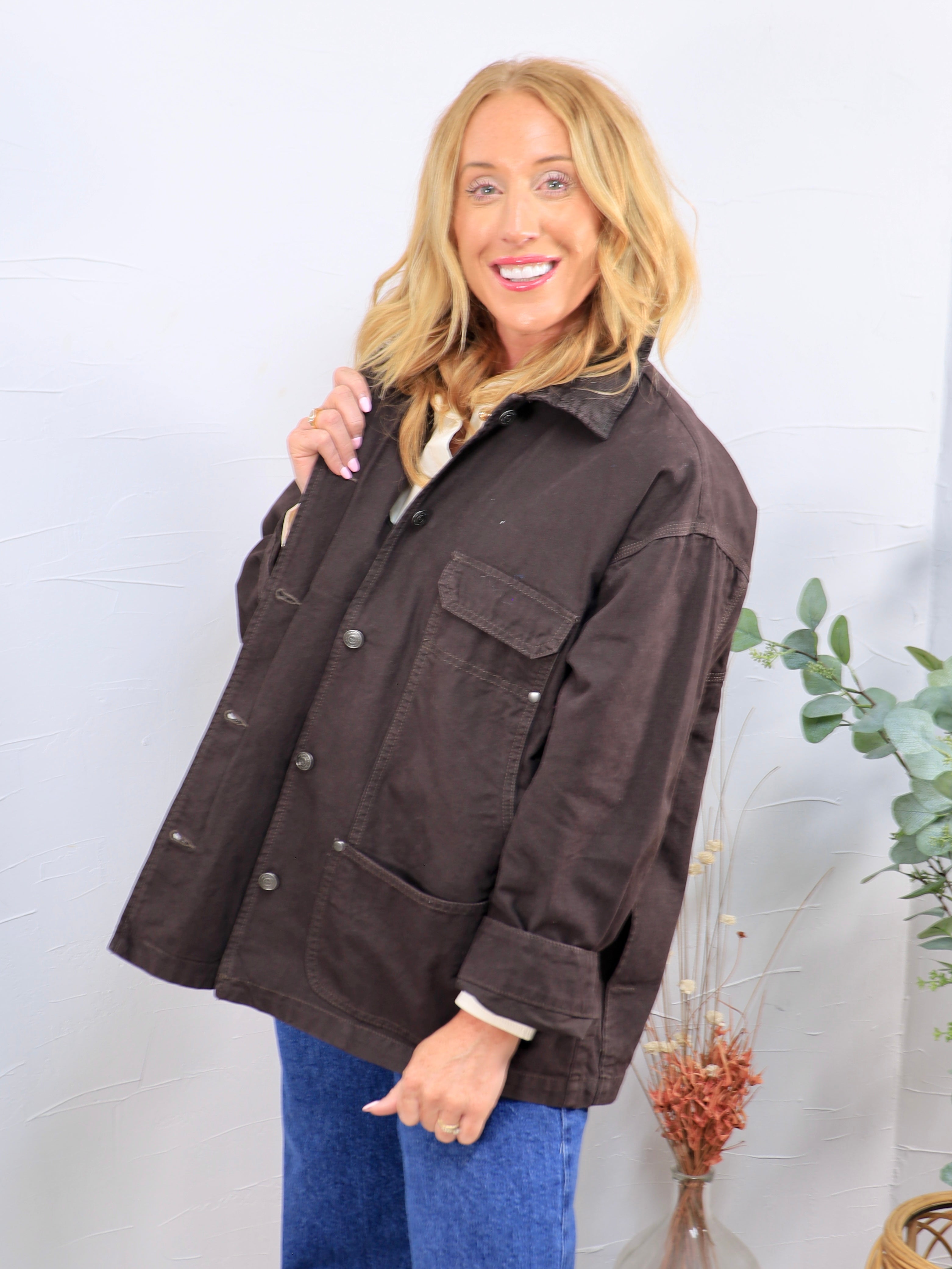 Oversized dark brown utility jacket with snap buttons, chest pocket, and sherpa lining, styled over blue jeans.