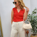 Woman wearing red sleeveless ribbed knit button-up top with cream wide-leg pants and sunglasses