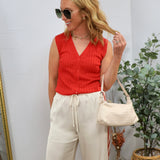 Woman wearing red sleeveless ribbed knit button-up top with cream wide-leg pants and sunglasses