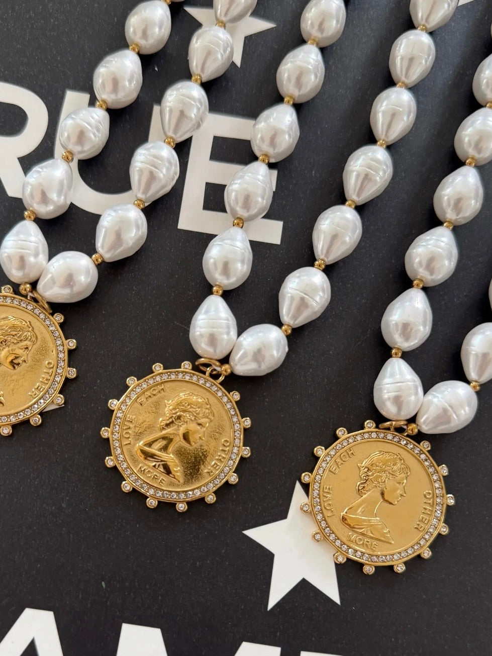 Pearl beaded necklaces with gold crystal-halo coin pendants engraved with Love Each Other More