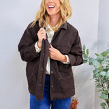 Dark brown oversized utility jacket with snap buttons, worn open over cream blouse and blue jeans.