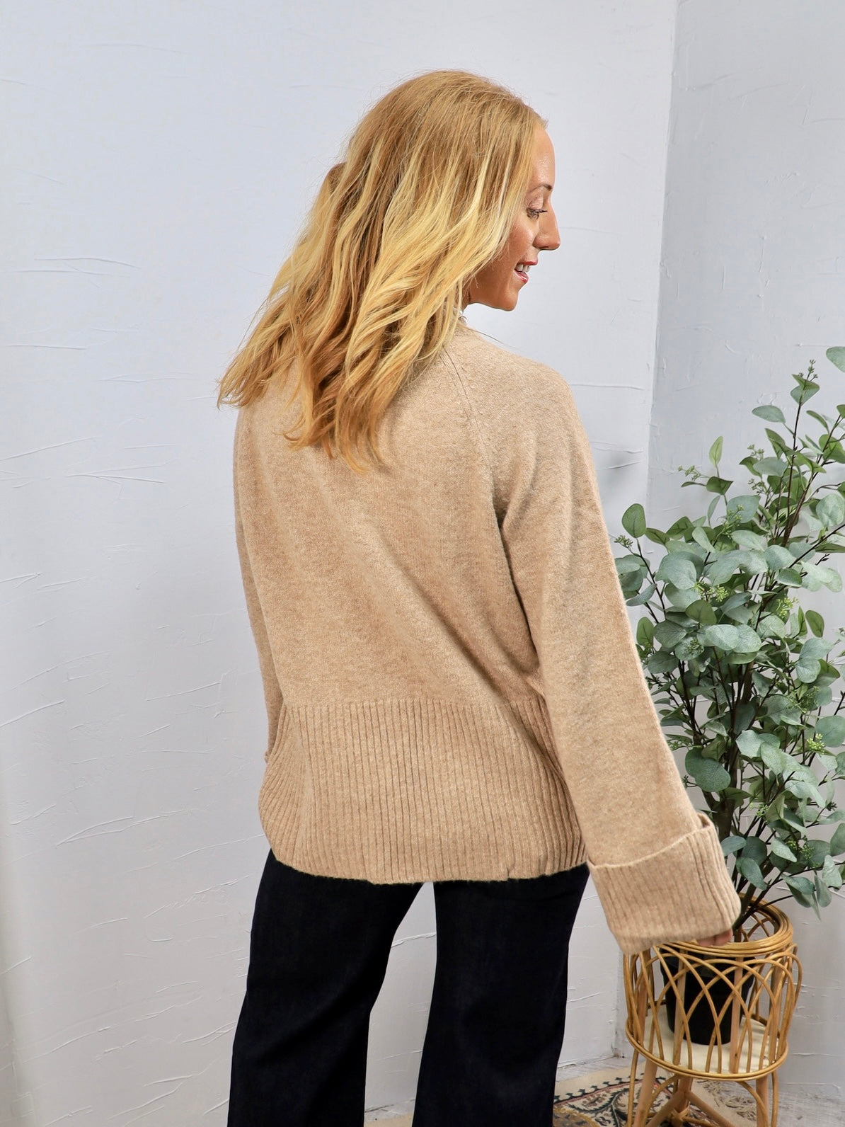Beige knit crewneck sweater with ribbed hem and cuffs, styled with black pants, back view.
