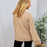 Beige knit crewneck sweater with ribbed hem and cuffs, styled with black pants, back view.