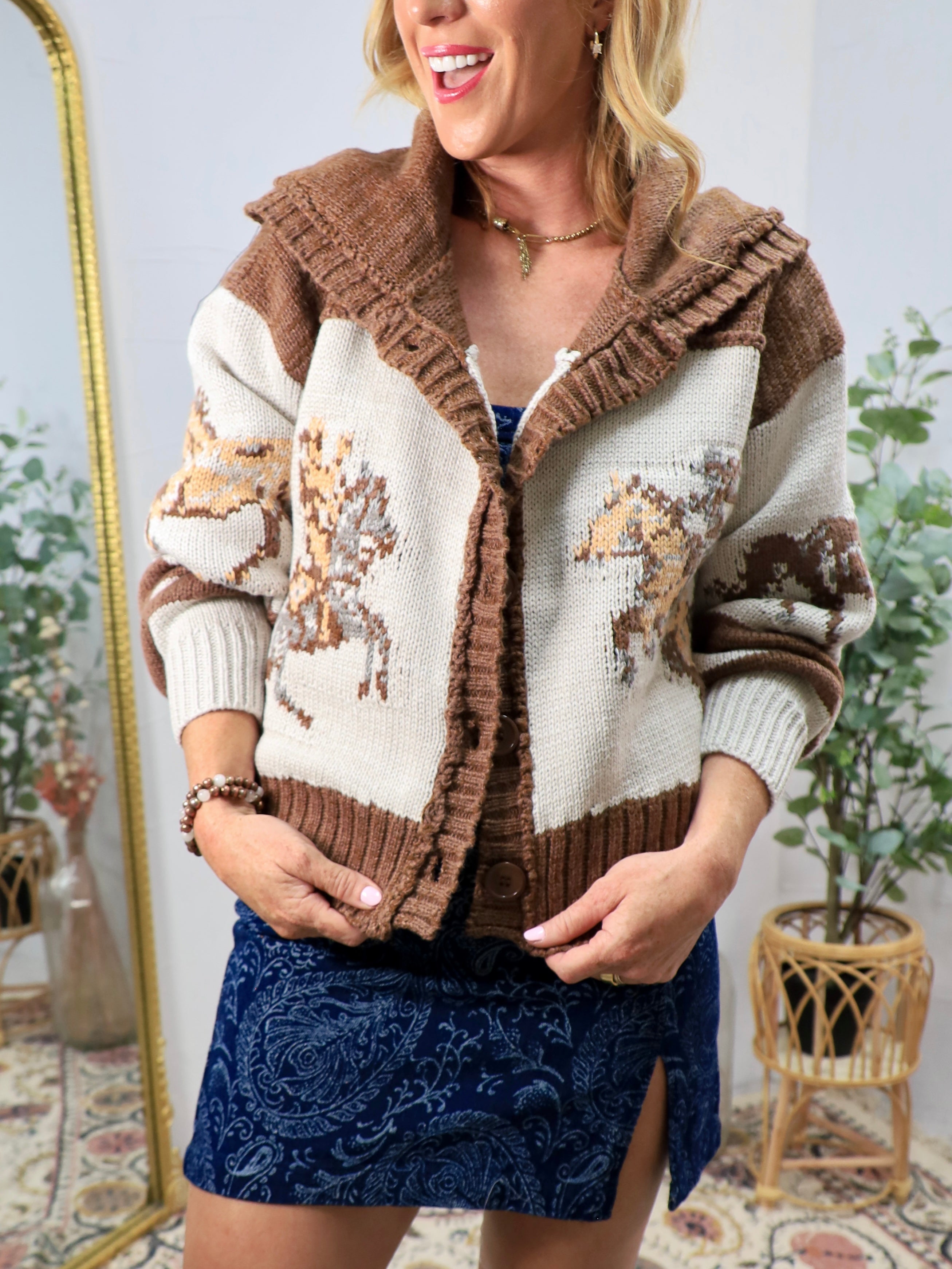 Woman wearing a cream and brown western horse-pattern knit cardigan sweater with ruffled hood and button front