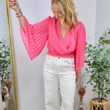 Hot pink wrap blouse with dramatic pleated bell sleeves, styled with white wide-leg jeans.
