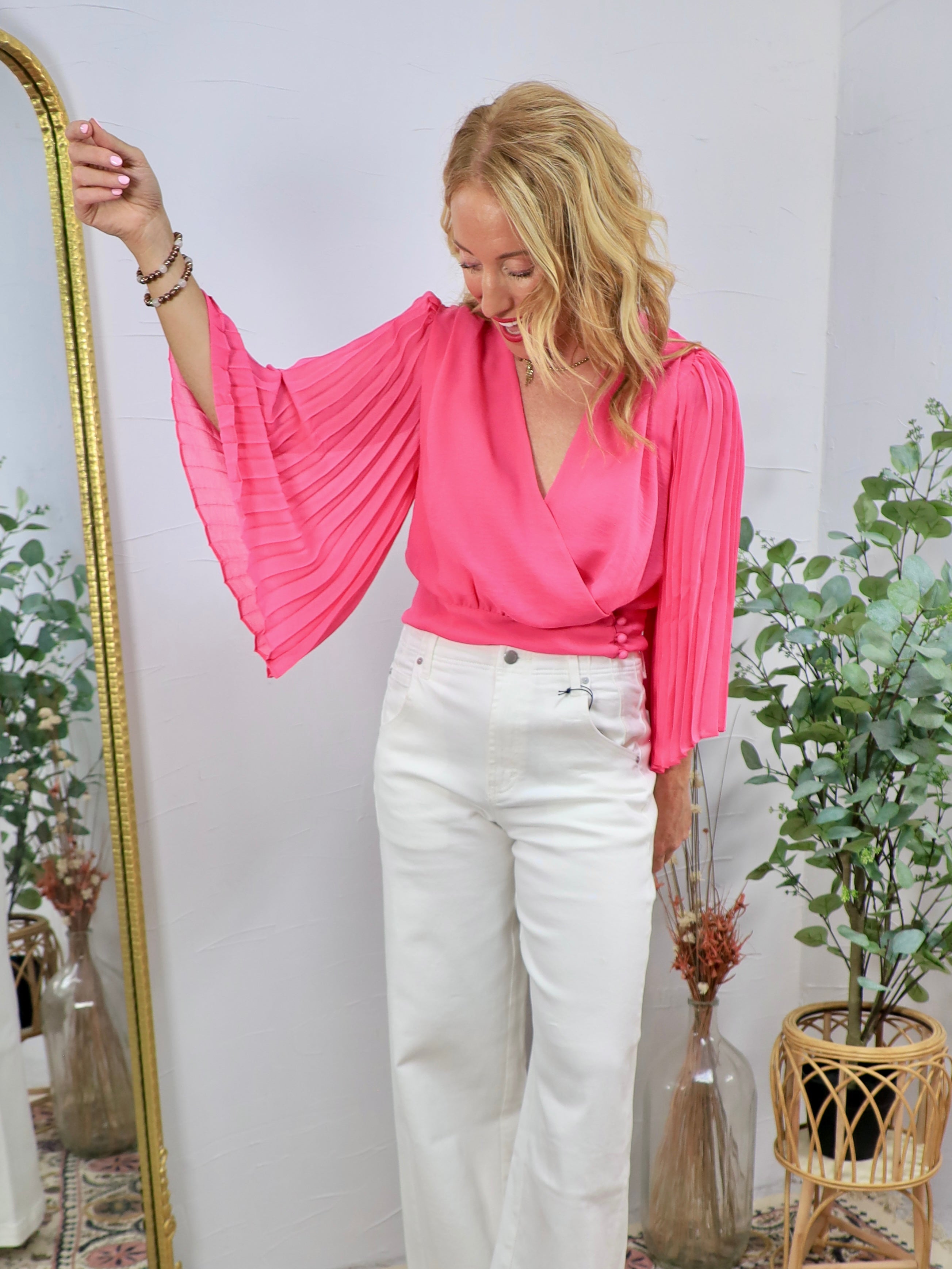 Hot pink wrap blouse with dramatic pleated bell sleeves, styled with white wide-leg jeans.