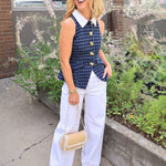 Navy blue gingham sleeveless vest with gold buttons and white collar, styled with wide-leg white trousers.
