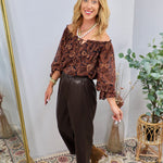 Dark brown faux leather tapered pants styled with paisley off-shoulder top and tan ankle boots.