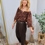 Dark brown faux leather tapered pants styled with paisley off-shoulder top and tan ankle boots.